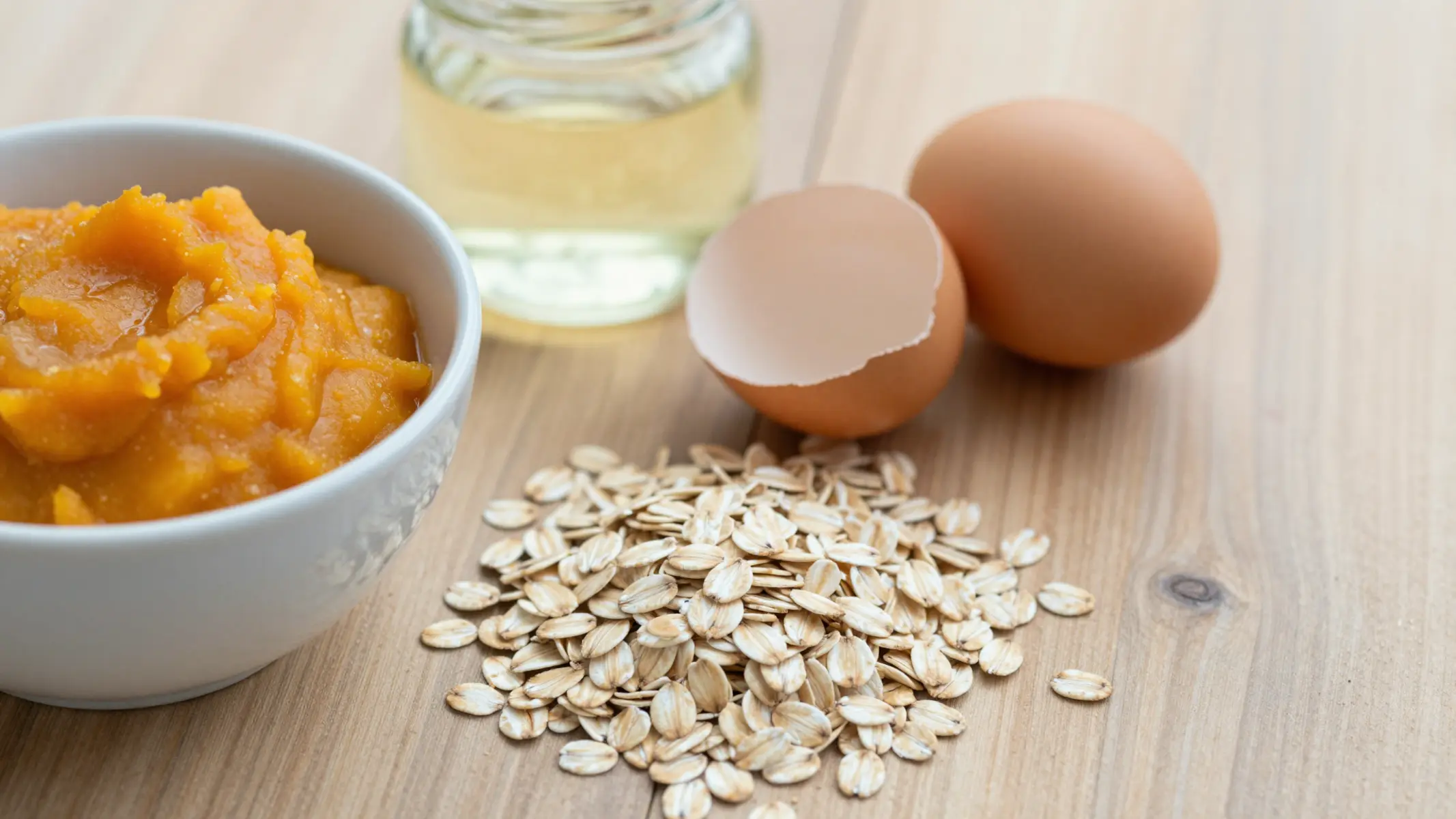 Ingredientes naturales sobre mesa de madera: puré de calabaza, avena, huevo y aceite de coco